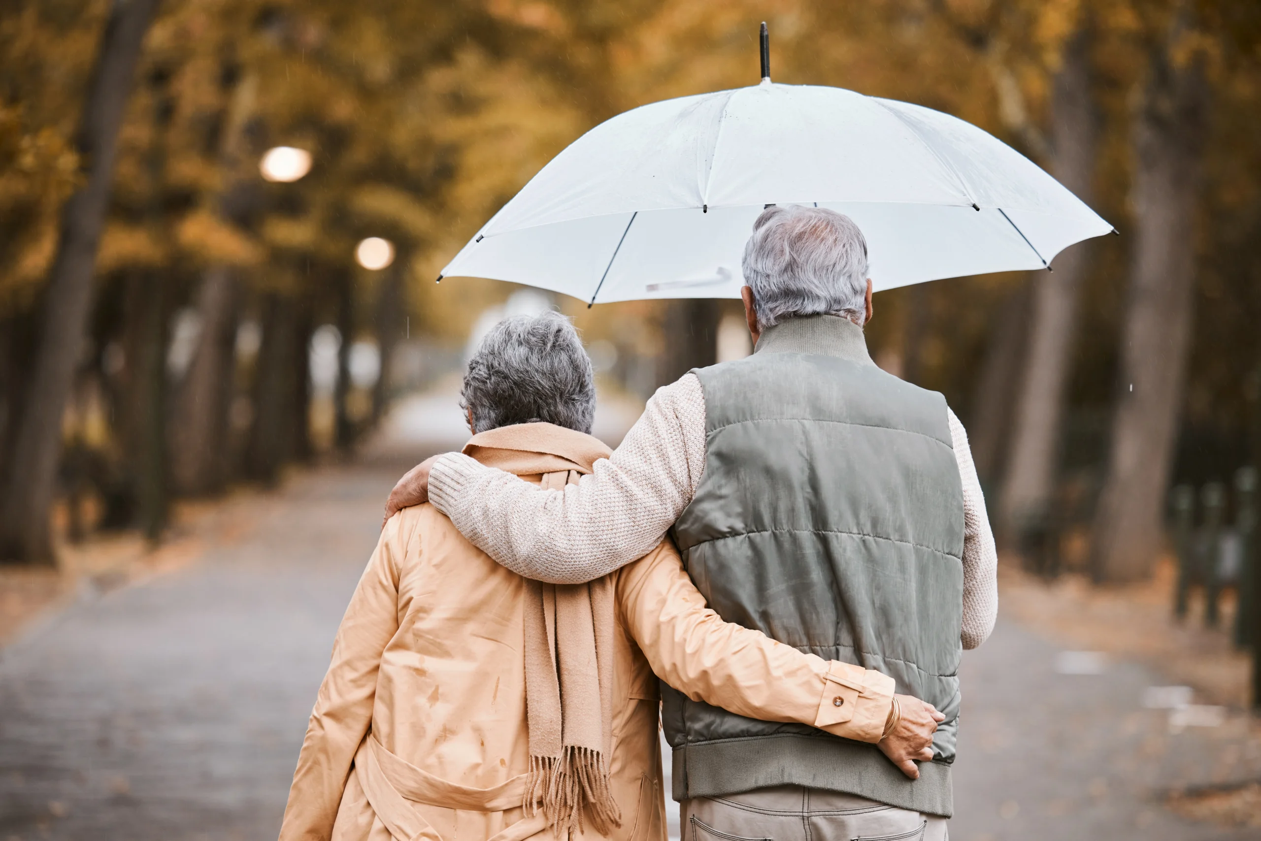 Elderly, couple walk in park with umbrella and fresh air, outdoor in nature in fall for exercise and retirement together.