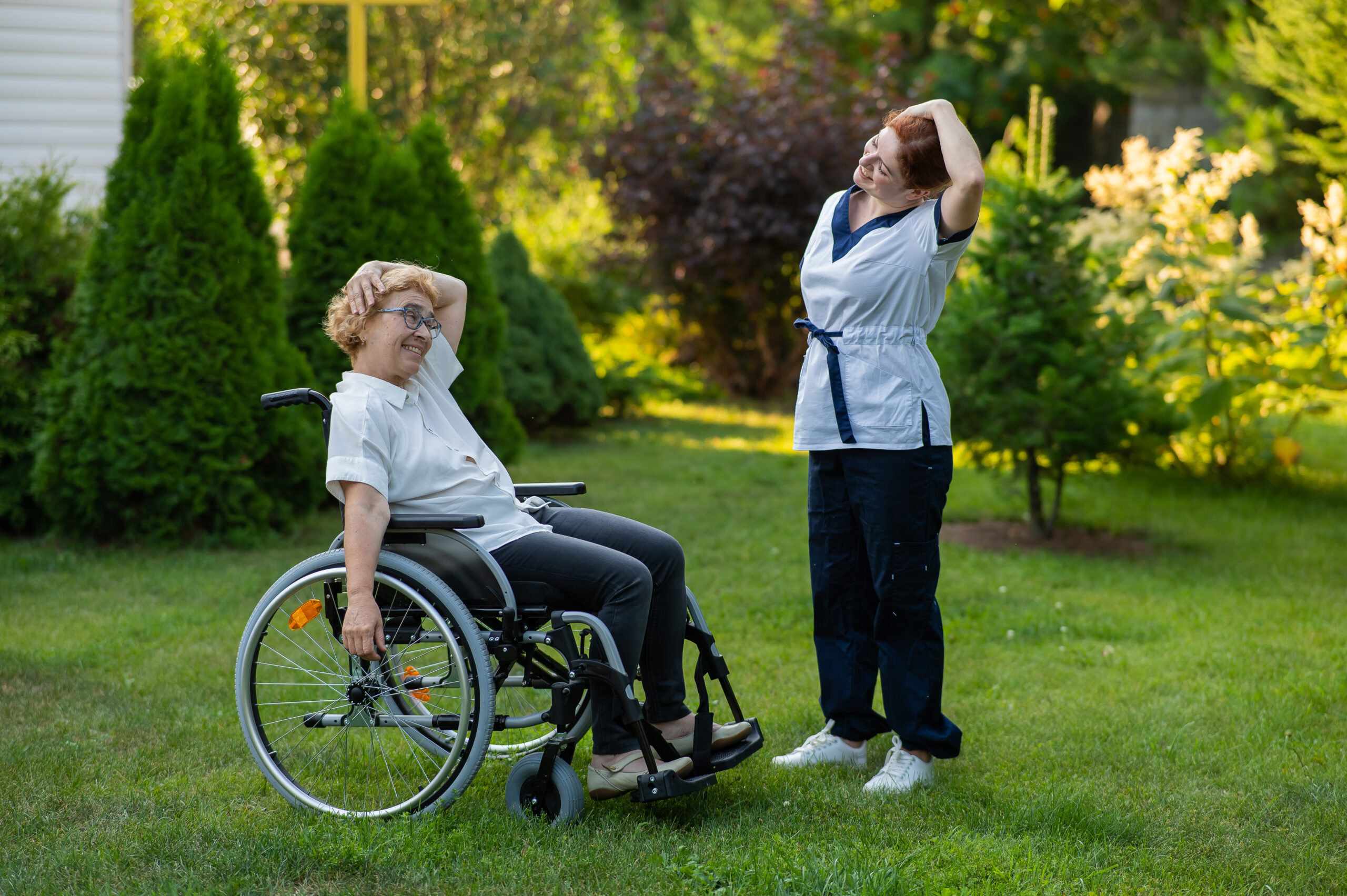 A nurse is exercising with an elderly patient in a wheelchair outdoors.